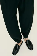 Mules estilo mocasín de cuero negro, con punta de almendra y detalle de tira penny con perforaciones decorativas en el empeine. Diseño destalonado con forro de punto.