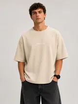 Remera de algodón pesado color beige, con diseño boxy, mangas cortas amplias y cuello redondo ribeteado. Cuenta con un pequeño estampado tipográfico en el pecho con la inscripción "BOHEMIANDESIGN®".