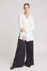 Camisa blanca de satén con cuello clásico, cierre frontal con botones y mangas largas.