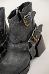 Botas cortas de cuero negro con acabado desgastado, punta cuadrada y taco bloque. Presentan un diseño versátil con estribo desmontable decorado con hebillas metálicas y tachas, permitiendo dos estilos diferentes en un mismo calzado.