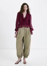 Blusa bordó de tejido fluido y semi transparente, con escote en V pronunciado, mangas largas abullonadas con volantes en los puños y detalles de volantes en el cuello y el ruedo.