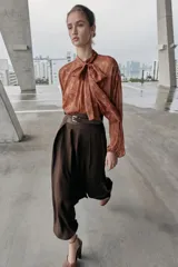 Camisa de estampado floral con cuello subido, lazo frontal y mangas largas con puños elásticos. Presenta un diseño con bajo asimétrico y cierre posterior con botones ocultos.