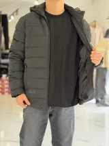 Campera puffer azul marino con capucha ajustable, cierre frontal y bolsillos laterales con cierre a presión. Cuenta con parche redondo con la inscripción "TURK" en el pecho.