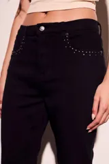 Pantalón de jean negro con corte flare, tiro medio y detalles de tachas plateadas en los bolsillos delanteros.