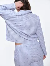 Camisa de dormir de popelina de algodón, con estampado de rayas verticales y pequeños motivos geométricos. Presenta cuello camisero, mangas largas y cierre frontal mediante lazos ajustables.