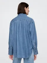 Camisa de jean de corte holgado, con cuello clásico, cierre frontal de botones y bolsillo en el pecho con logo bordado. Presenta mangas largas con puños anchos.