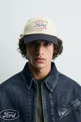 Gorra de seis paneles, color beige, con visera azul marino. Presenta bordado frontal con el texto "Genuine Ford Parts" en tonos azul y rojo, y un pequeño parche bordado con el logo de Ford en el lateral.
