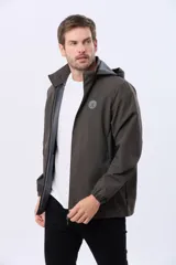 Campera repelente al agua y cortaviento color marrón oscuro, con capucha desmontable y cierre frontal. Cuenta con bolsillos y puños elastizados, además de un parche redondo en el pecho.