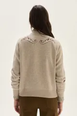 Sweater de tejido de punto color beige con diseño de arabescos en tonos marrones en hombros y mangas. Presenta cuello redondo con cordones decorativos y puños con textura acanalada.