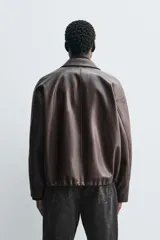 Cazadora de corte relajado confeccionada en tejido efecto piel color marrón oscuro. Presenta cuello solapa, cierre frontal con cremallera oculta por solapa con botones a presión, bolsillos de plastrón con solapa en la parte frontal y bajo ajustable con elástico en los laterales.