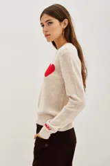 Sweater de punto color beige, con cuello redondo y manga larga. Presenta un corazón rojo bordado en el pecho y la palabra 'l'amour' bordada en el puño de la manga.