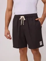 Bermuda de corte recto en color beige, confeccionada en una mezcla de algodón, lino y poliéster. Presenta cintura elástica con cordón ajustable, bolsillos laterales y una pequeña etiqueta decorativa en el ruedo.