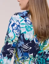 Blusa de gasa estampada de la marca Zac & Rachel, con diseño floral en tonos azul, celeste y verde sobre base blanca. Presenta escote en V con abertura y botones frontales, y mangas largas de largo regulable con presilla.