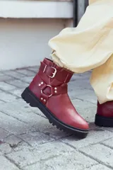 Bota corta de cuero color borgoña, con suela track negra, puntera redondeada y múltiples correas con hebillas plateadas.