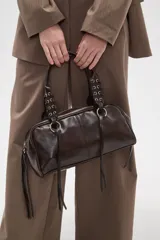 Bolso tipo bowling color negro de poliuretano, con doble asa corta decorada con argollas y tiritas colgantes en los laterales.