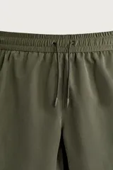 Short de baño largo en color beige, confeccionado en tejido técnico con tacto aterciopelado. Cuenta con cintura elástica ajustable con cordón, bolsillos laterales y detalle de bolsillo trasero, además de forro interior.
