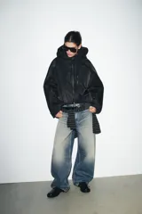 Chaqueta acolchada de color negro con acabado repelente al agua y resistente al viento. Presenta cuello subido con capucha ajustable, cierre frontal con cremallera termosellada, bolsillos delanteros con cremallera y bajo con ajuste elástico. Las mangas largas cuentan con tiras adhesivas ajustables en los puños.
