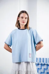 Remera de algodón color celeste claro con cuello redondo y bordes de manga en contraste azul marino. Los bordes de las mangas tienen un detalle de pespunte decorativo en color azul. Posee un pequeño parche bordado en la parte inferior izquierda.