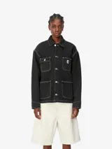 Campera de trabajo tipo chore coat Carhartt modelo Michigan, confeccionada en denim negro con costuras en contraste. Presenta cierre frontal con botones metálicos grabados, cuello clásico y cuatro bolsillos frontales, uno de ellos con etiqueta de la marca.