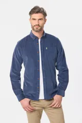 Camisa de pana fina en color verde oscuro, de manga larga con puños arremangados, cuello camisero con botones y un bolsillo aplicado en el pecho con pequeña etiqueta decorativa.