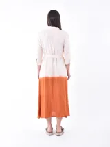 Vestido camisero midi de lino con diseño bicolor, presentando una parte superior en color crudo y una parte inferior en color naranja con efecto degradado. Posee cuello camisero, cierre frontal con botones y un lazo ajustable en la cintura del mismo tono que la parte inferior.