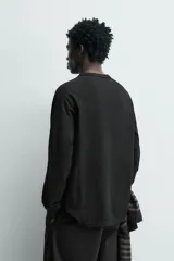 Camiseta de manga larga tipo ranglán con cuello redondo y cierre frontal de botones. Presenta un diseño de rayas horizontales finas en tonos oscuros.