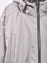 Campera gris con capucha con borde de piel sintética, cierre frontal con cremallera, bolsillos laterales con solapa y bolsillo con cremallera en la manga.