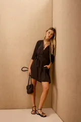 Vestido corto de color negro, con mangas tres cuartos, cuello mao y cierre frontal con botones. Incluye un lazo a tono para ajustar en la cintura y bolsillos laterales.