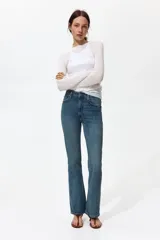 Jean de tiro alto y corte bootcut, confeccionado en denim de algodón levemente elástico con lavado azul medio y efecto desgastado. Presenta diseño clásico de cinco bolsillos, cierre de cremallera y botón metálico.