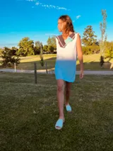 Vestido corto tejido en hilo de algodón color celeste, con cuello y espalda con apliques de cuero artesanal en tonos marrón, blanco y celeste.