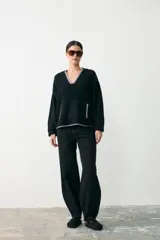 Sweater de textura bouclé color negro con detalles de ribete en color gris en el escote en V, puños y bolsillos frontales. Presenta un diseño de manga larga y corte holgado.