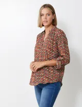 Blusa de gasa con estampado geométrico en tonos tierra (marrón, rojo, verde, amarillo). Presenta cuello solapa con escote en V y mangas largas ajustables con presilla y botón.