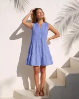 Vestido corto de lino natural color blanco, sin mangas, con cuello mao y escote en V con botones de nácar. Presenta diseño escalonado con volados fruncidos en la falda.