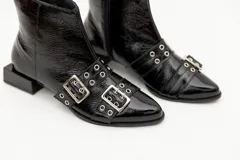 Botas cortas de cuero charol color negro, con aplique de hebillas con ojalillos y cierre lateral. Taco cuadrado bajo.