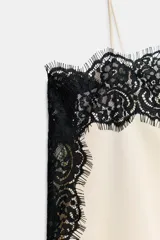 Top lencero de escote recto y tirantes finos, color crema, con aplicación de encaje negro contrastante en todo el contorno. Presenta aberturas laterales en el bajo.