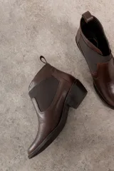 Botín negro de cuero con elásticos laterales, taco bajo y tirador trasero.