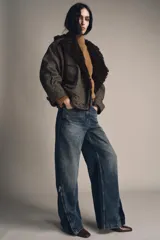 Jeans de mezclilla azul oscuro con efecto lavado, tiro medio y corte balloon (pierna ancha y holgada). Presenta cinco bolsillos y cremalleras metálicas decorativas que recorren la parte exterior de las piernas desde el muslo hasta el bajo.