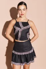 Top negro de breteles finos con diseño estructurado y detalles de volados en tela brillante plateada aplicada en forma de cruz sobre el frente.