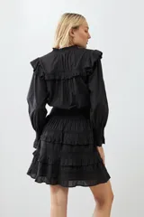 Vestido corto negro con escote en V, mangas largas abullonadas con puños elásticos, falda con volados y cinturón trenzado.