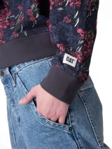 Buzo Caterpillar de cuello redondo en suave tejido french terry, de calce relajado y mangas largas. Presenta estampado floral completo en tonos azules y rojos, con el logo de la marca en el centro del frente y detalles de punto acanalado en puños, cuello y dobladillo.