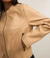 Campera básica de cuero sintético (PU) color marrón oscuro, con cuello redondo, cierre frontal y recortes decorativos. Cuenta con mangas largas y bolsillos con cierre.