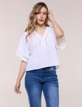 Blusa blanca de poliéster con textura crepada, escote en V con detalles de puntilla, mangas cortas amplias estilo kimono y diseño semi entallado bajo el busto con faldón suelto.