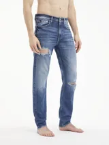 Jeans de algodón elástico, lavado a la piedra azul oscuro, con talle medio y pierna estrecha en el tobillo. Presenta roturas en ambas piernas.