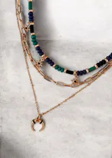Set de collares tipo cascada en color dorado, compuesto por tres niveles: una gargantilla de cuentas multicolor con dijes de estrellas, una cadena de eslabones y una cadena fina con dije de medialuna.
