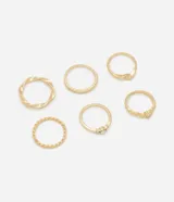 Set de seis anillos de metal con baño en tono dorado, que incluye diversos diseños como texturas trenzadas, bandas lisas y detalles con incrustaciones de strass.