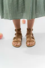 Sandalia gladiadora color marrón claro de cuero sintético, con múltiples tiras y hebillas metálicas ajustables. Base de corcho y plantilla anatómica forrada en eco-cuero.