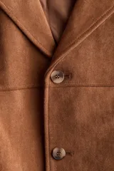Campera marrón de tejido suave con acabado cepillado, solapas de muesca, cierre frontal de botones, bolsillos laterales insertados y canesú delantero y trasero.