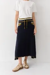 Falda midi de lana en color azul marino, con diseño acanalado y silueta amplia. Presenta una cintura elástica con cordón ajustable, detalles de rayas en tonos verde oliva y crema en la parte superior, y bolsillos laterales.