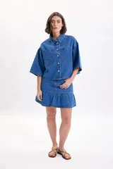 Sobrecamisa de jean de manga corta y corte oversize en color azul medio, con bolsillos frontales con solapa y cierre de botones metálicos a presión.