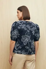 Blusa azul marino con bordados calados en color blanco. Presenta escote en pico, mangas abullonadas con puños elásticos y un diseño de ajuste relajado.